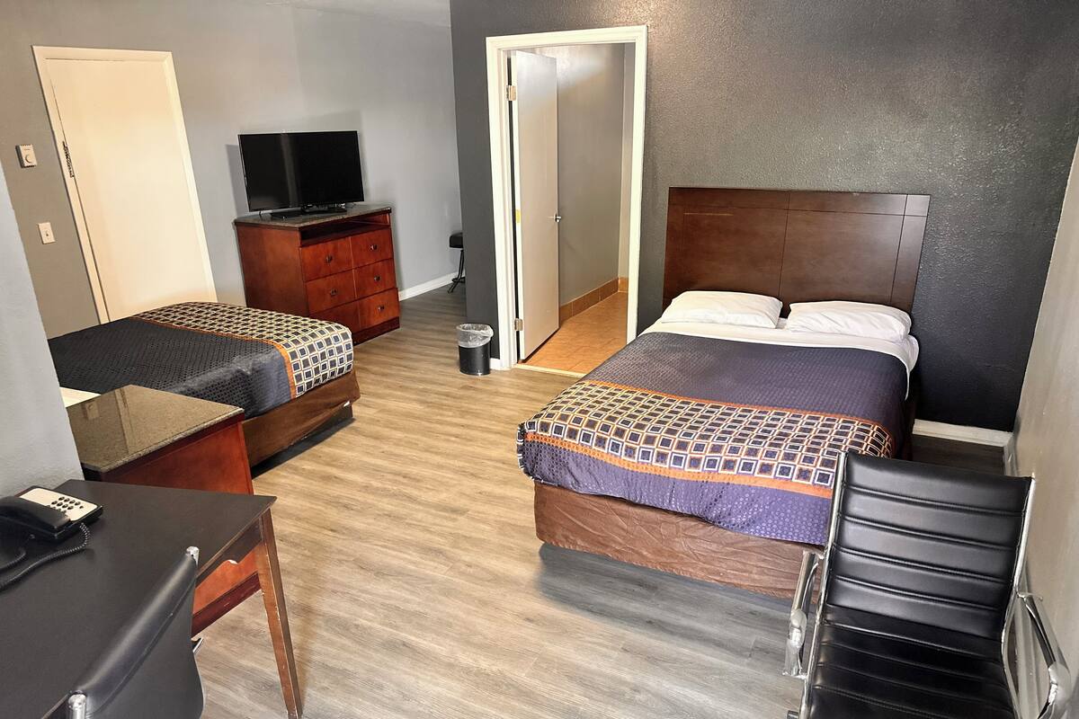 A hotel room with two beds, a desk, a chair, a TV, and a trash bin.