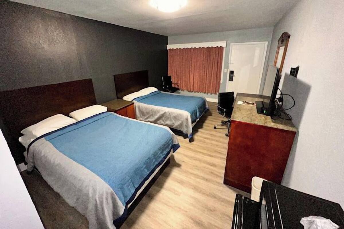 A hotel room with two beds, a desk, a chair, a television, and a mirror.