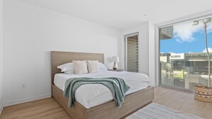 A bedroom with a wooden bed, white bedding, a bedside lamp, and a view of a building through the window.