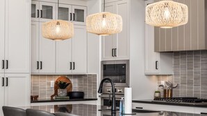 A modern kitchen with white cabinets, a central island with bar stools, and two woven pendant lights. - Adventure Central at Desert Color (by Ember Stays) (St. George)