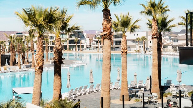 A pool area with palm trees, lounge chairs, and a clear sky. - Adventure Central at Desert Color (by Ember Stays) (St. George)