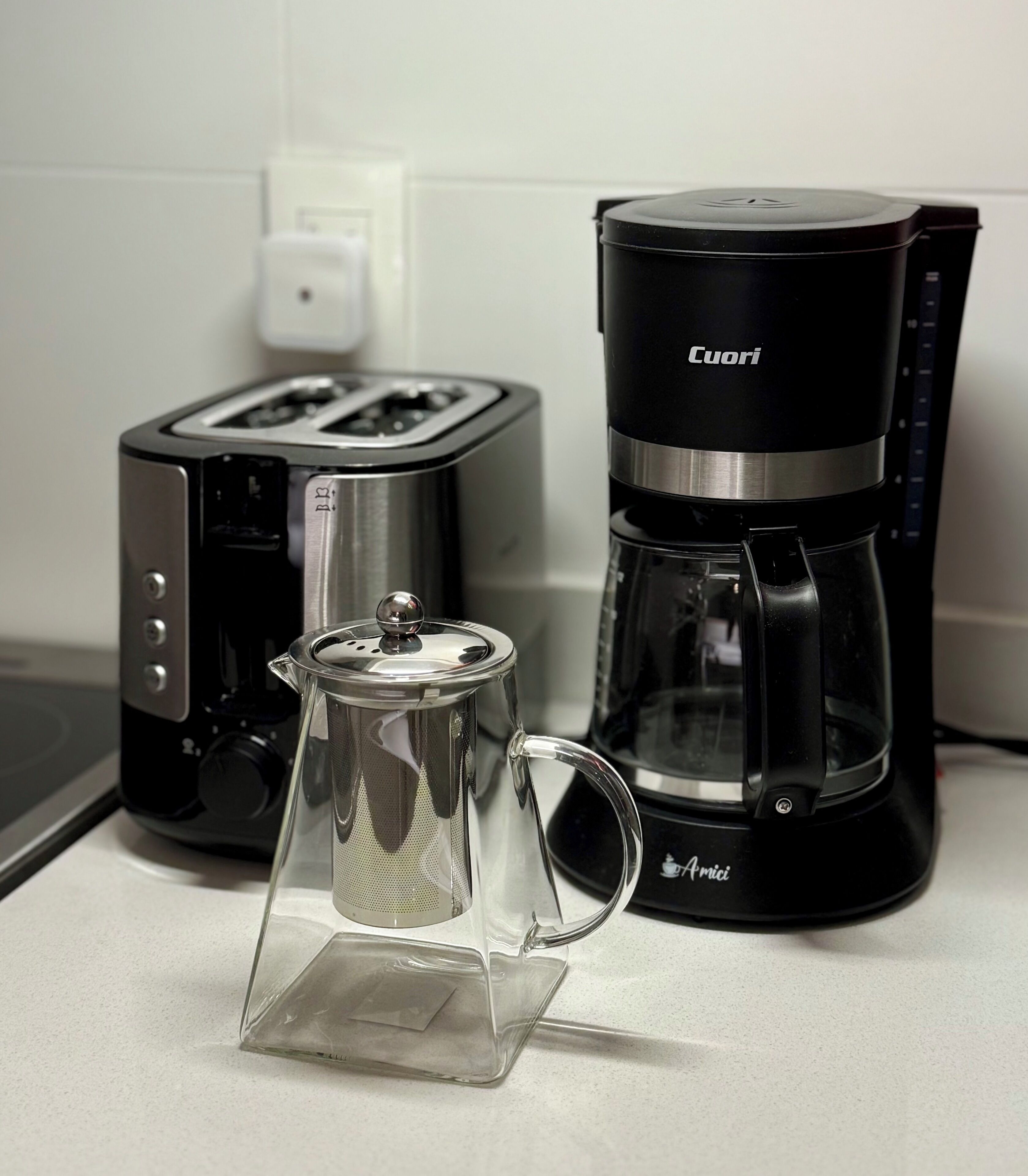 Une cuisine avec une machine à café noire, une cafetière en verre et un grille-pain.