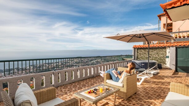 A rooftop terrace with wicker furniture, a table with fruit and drinks, and a view of the city and sea. - Skyline Heights by Madeira Sun Travel (Funchal)