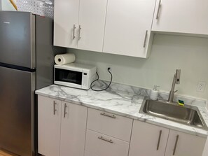 Una cucina con mobili bianchi, un frigorifero in acciaio inossidabile, un forno a microonde e un lavello con rubinetto.