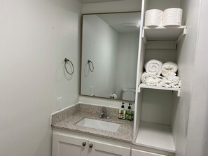Een badkamer met een wastafel, spiegel, handdoekrek en planken met handdoeken.