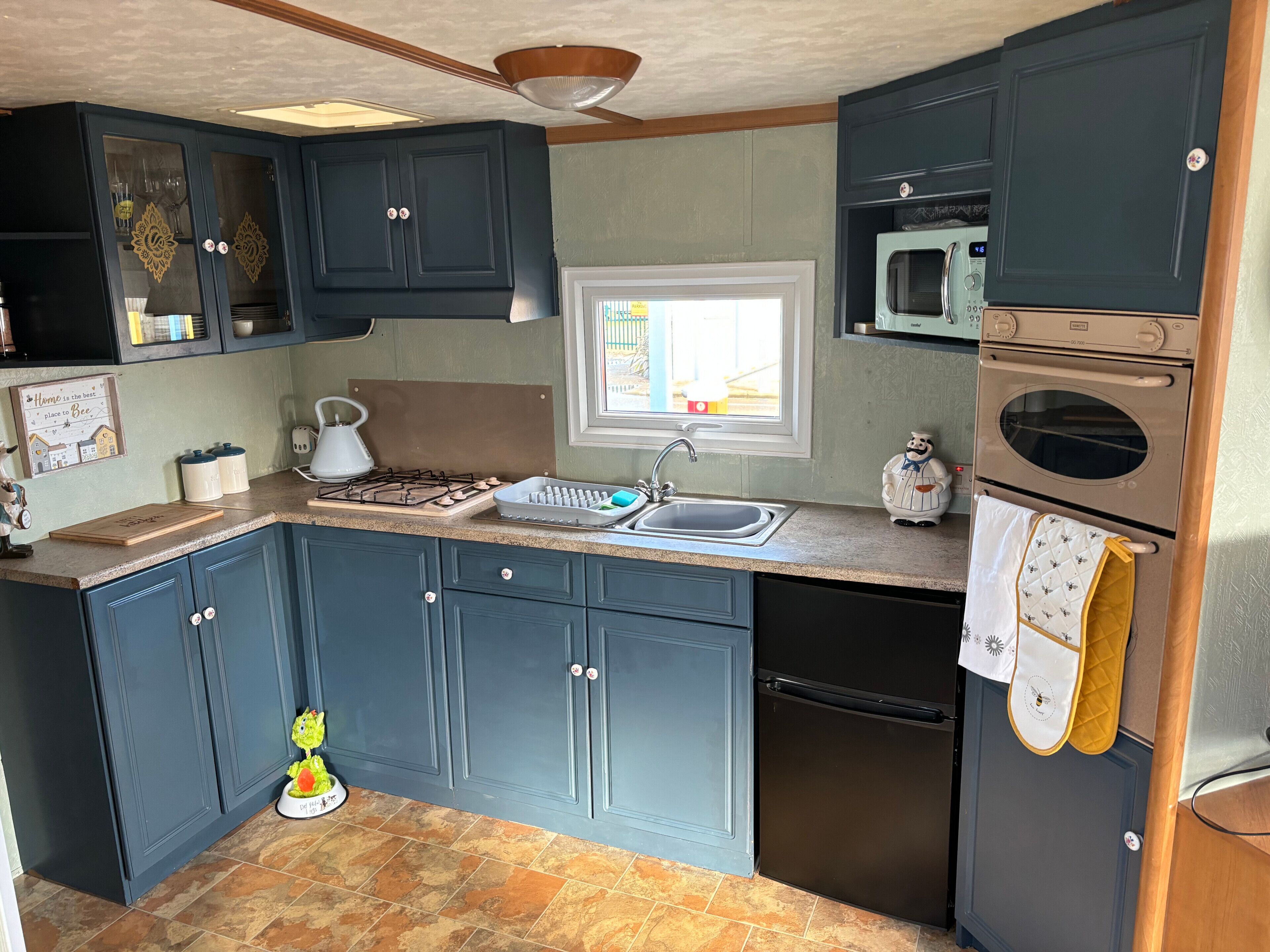 A compact kitchen with dark blue cabinets, a gas stove, a sink, a microwave, and a refrigerator.