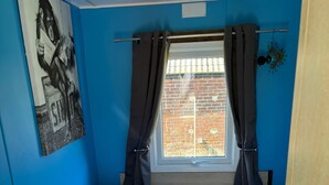 Una habitación con dos camas, una ventana con cortinas, un cuadro en la pared y un muro de ladrillos afuera.