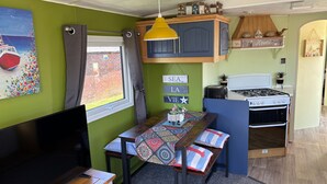 Una cocina compacta con estufa, una mesa de comedor con sillas, un televisor y una ventana con cortinas.