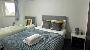 A double bed with a grey headboard, two bedside tables, a window with curtains, and a bedside lamp. - 1BR-Sleeps4-Parking-ClosetoCentre (Birmingham)