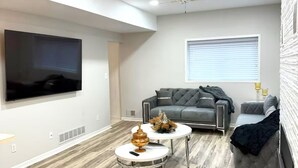A modern living room with a flat-screen TV, grey sofa, round coffee table, and a ceiling fan. - Charming 3-bedroom house in peaceful White Lake Township on Pontiac Lake (White Lake Township)