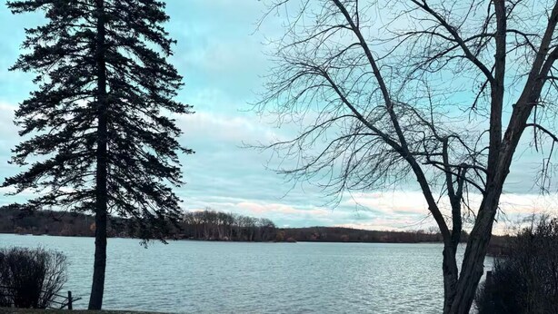 A paved walkway leading to a lake with snow on the ground and trees in the background. - Charming 3-bedroom house in peaceful White Lake Township on Pontiac Lake (White Lake Township)