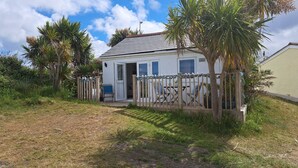 A small, single-story house with a white exterior, a wooden deck, and a fenced patio area.