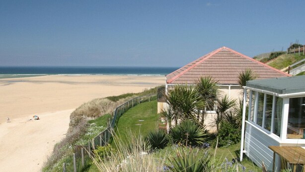 A beachfront property with a sandy beach, a fenced area, and a building with a red roof.