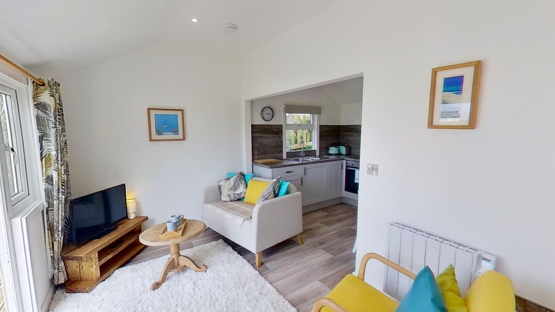 A compact living space with a sofa, a small table, a TV, and a kitchen area with a window.