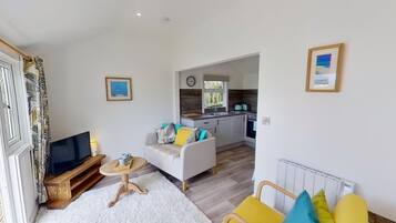 A compact living space with a sofa, a small table, a TV, and a kitchen area with a window.