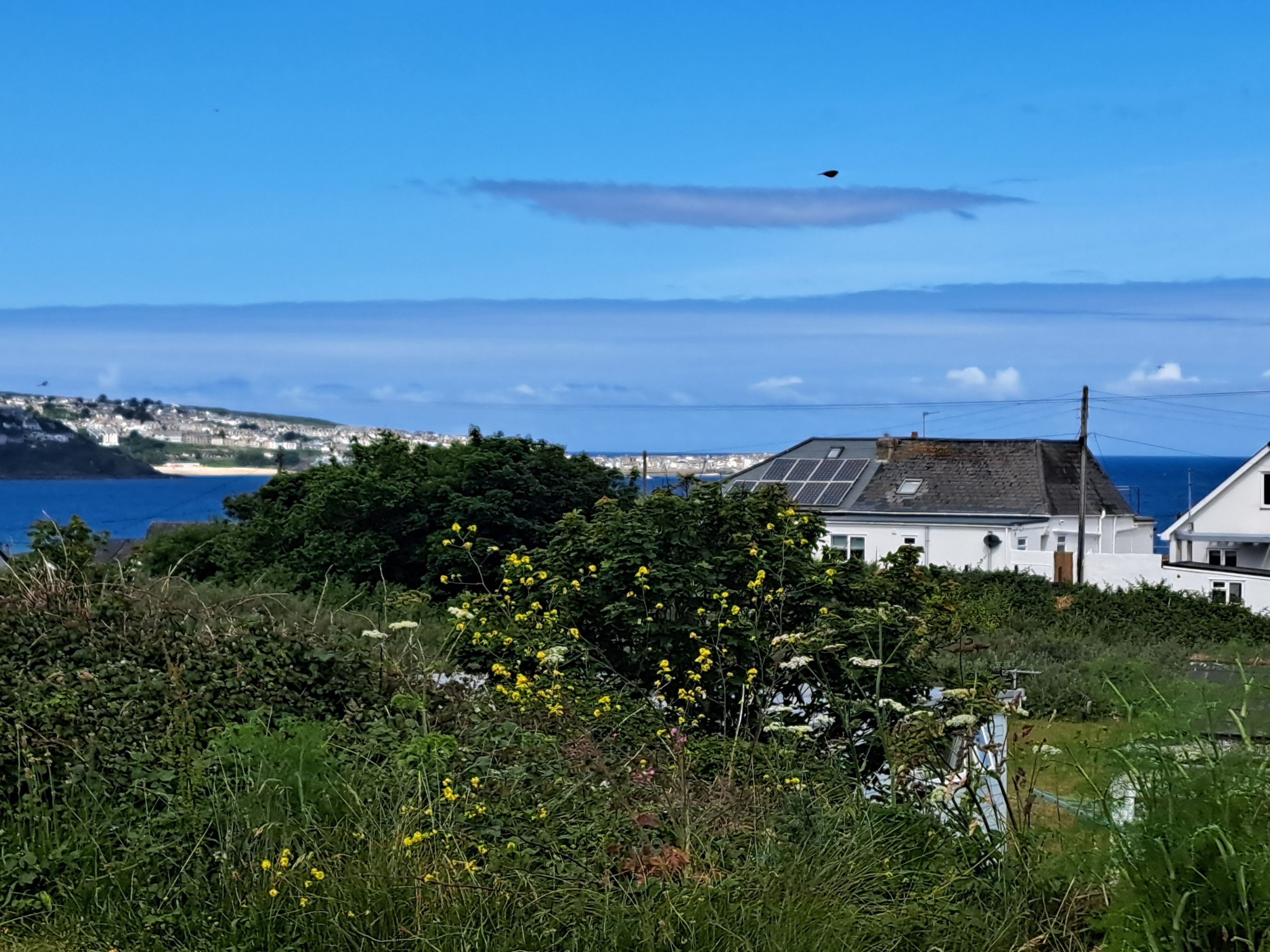 Een huis aan de kust met uitzicht op zee en heuvels op de achtergrond.