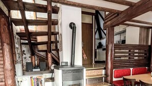 A cozy interior with a modern fireplace, wooden beams, a dining area with red upholstered chairs, and a staircase leading to another level.