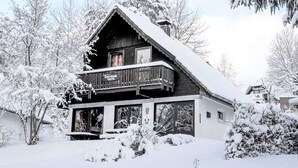 A wooden chalet with a balcony, surrounded by snow-covered trees.