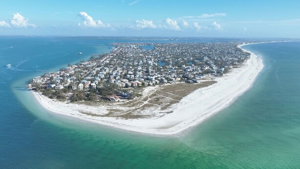 Vista aérea de una zona residencial costera con una extensa playa de arena y aguas azul turquesa.