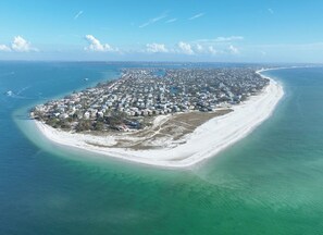 Oversigtsbillede af et kystnære boligområde med en lang sandstrand og klart, blåt vand.