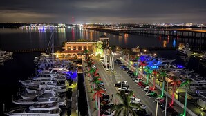 Un puerto deportivo de noche con barcos amarrados, un puente al fondo y un paisaje urbano al otro lado del agua.