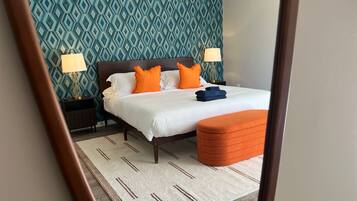 Un lit bien fait, avec une literie blanche et orange, un pouf assorti de la même couleur et un mur à motifs en arrière-plan.