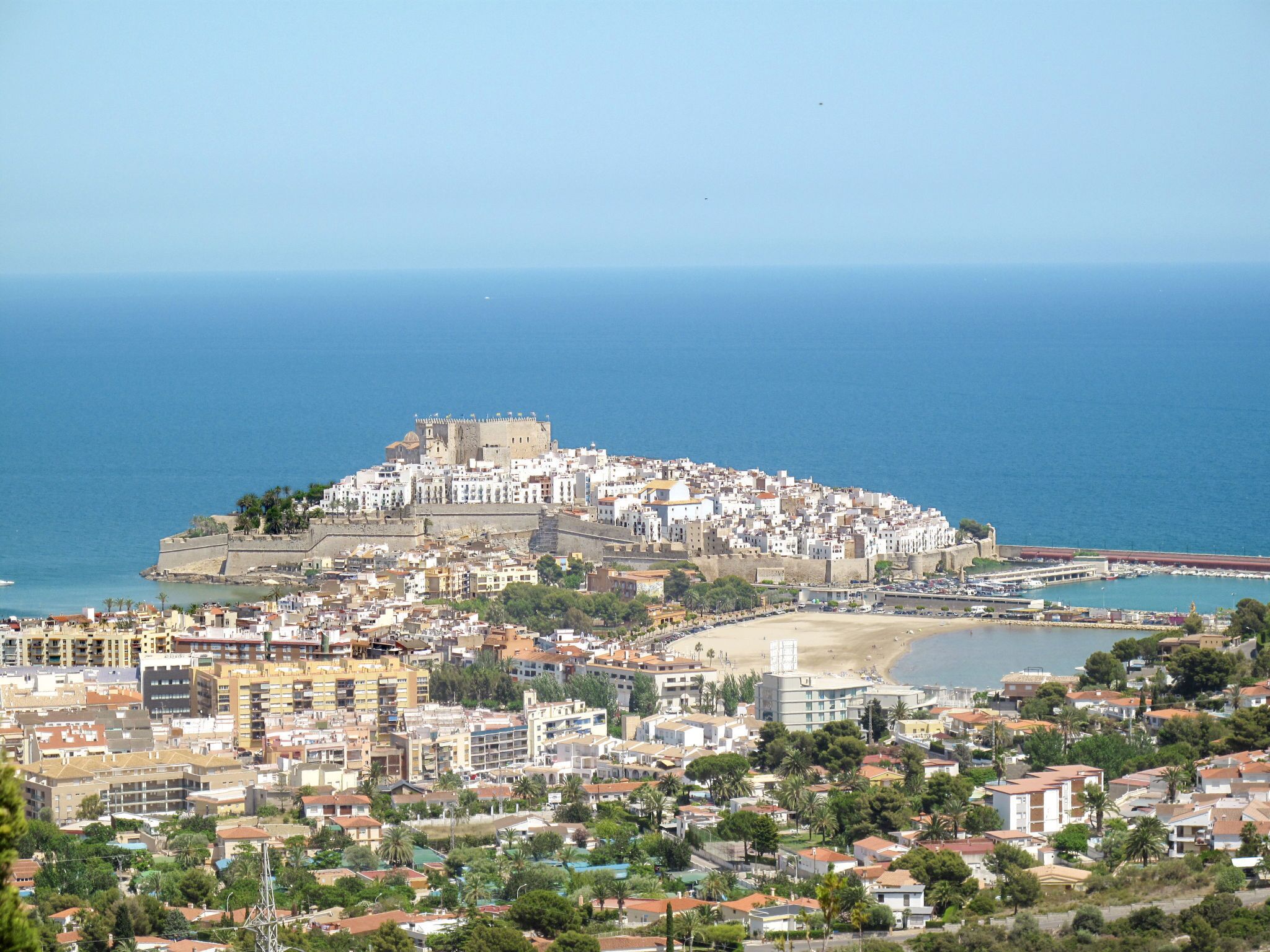 A coastal cityscape with a prominent hilltop fortress, a beach, and dense residential buildings.