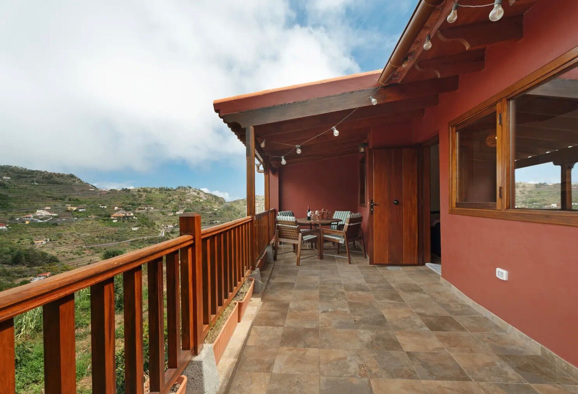 Un balcone con ringhiera in legno, un tavolo con sedie e vista su un paesaggio collinare.