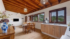 A spacious kitchen with wooden cabinets, a dining area with chairs, large windows with a view, and a wooden ceiling. - 'Tilo' Apartment with Mountain Views, Wi-Fi and Air Conditioning - SilboHolidays (Santa Cruz de Tenerife.)