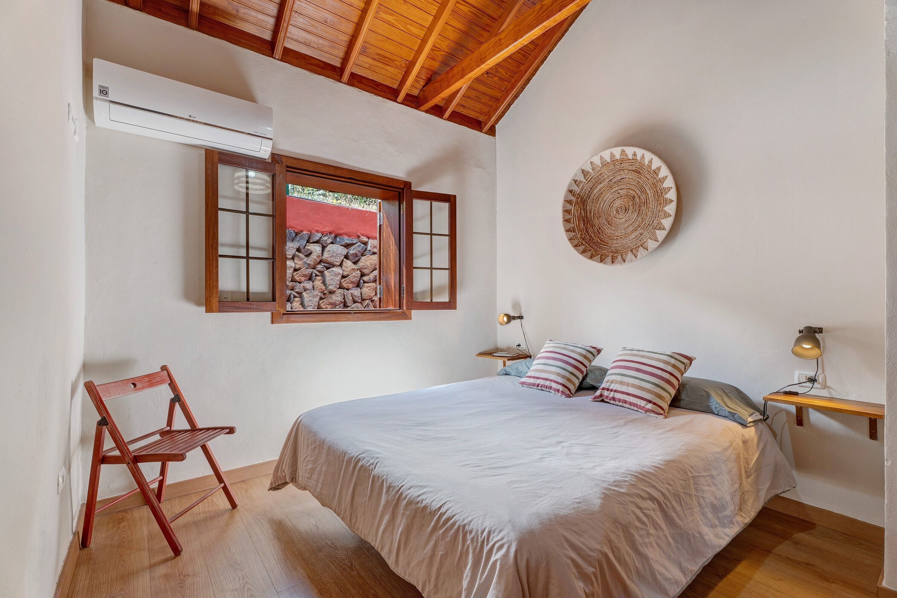 Una camera da letto con un letto, pavimento in legno, una finestra vista rocce, condizionatore d'aria a muro e un piatto decorativo.