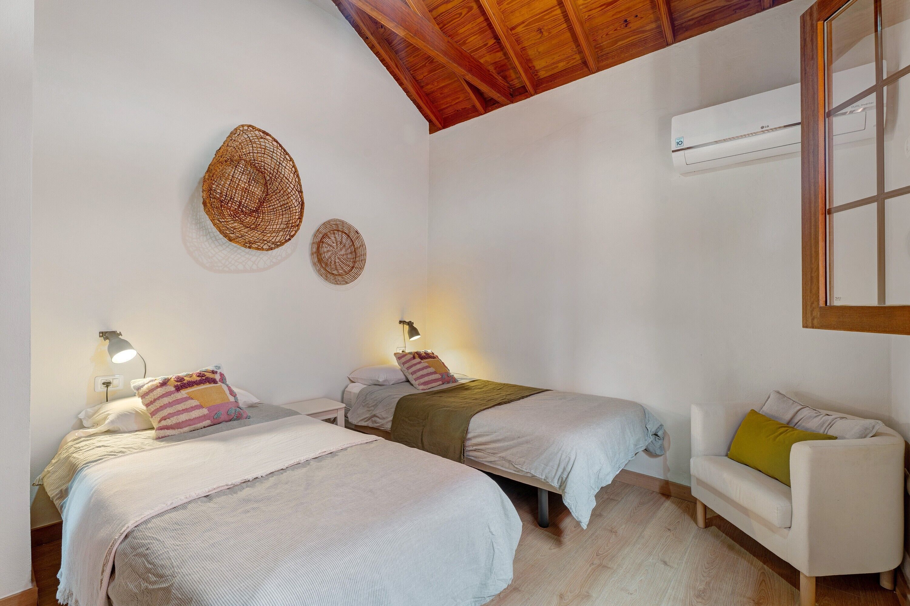 Een slaapkamer met twee bedden, een witte bank, een airconditioner en een houten plafond.