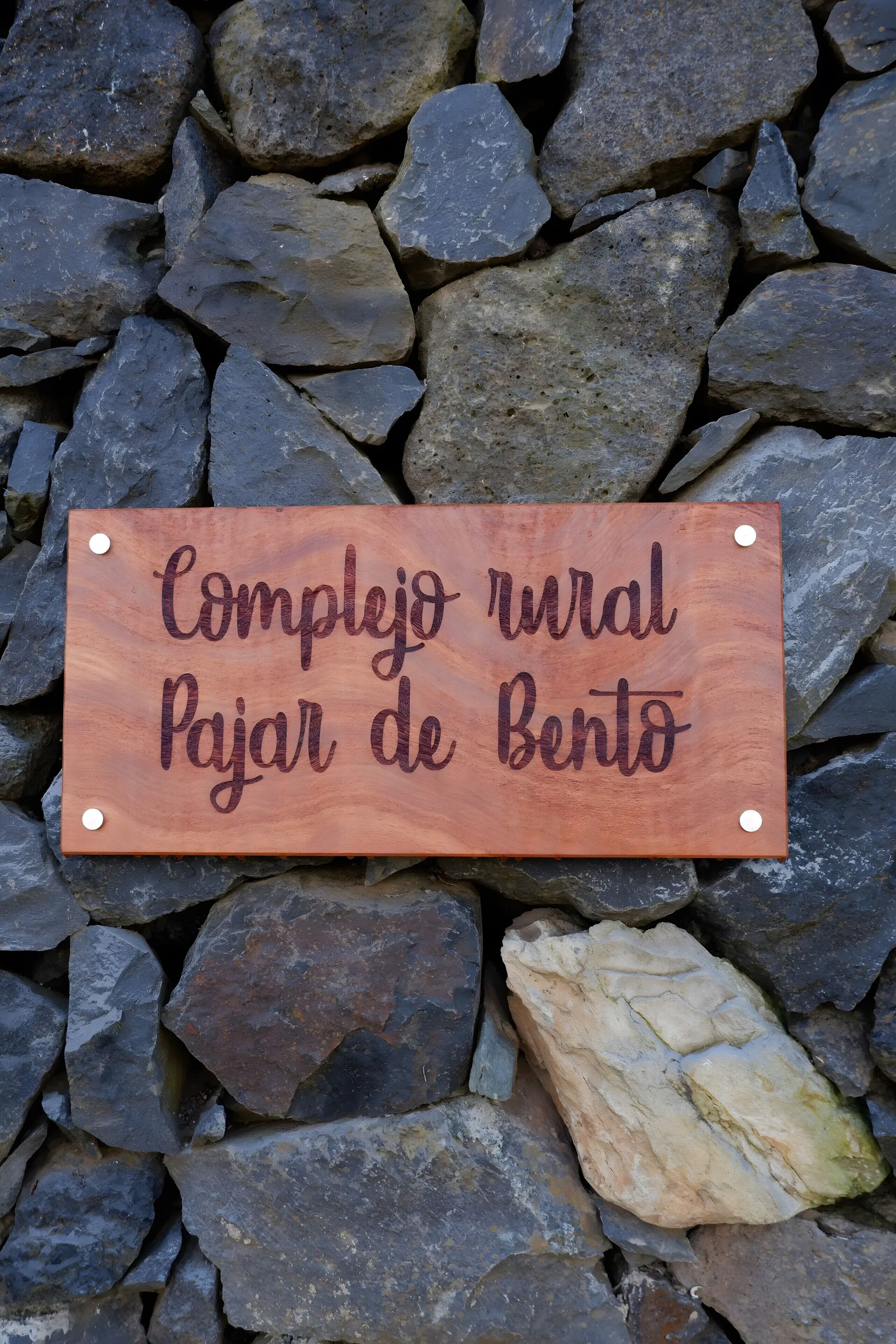 A wooden sign with text on it, placed on a bed of rocks.