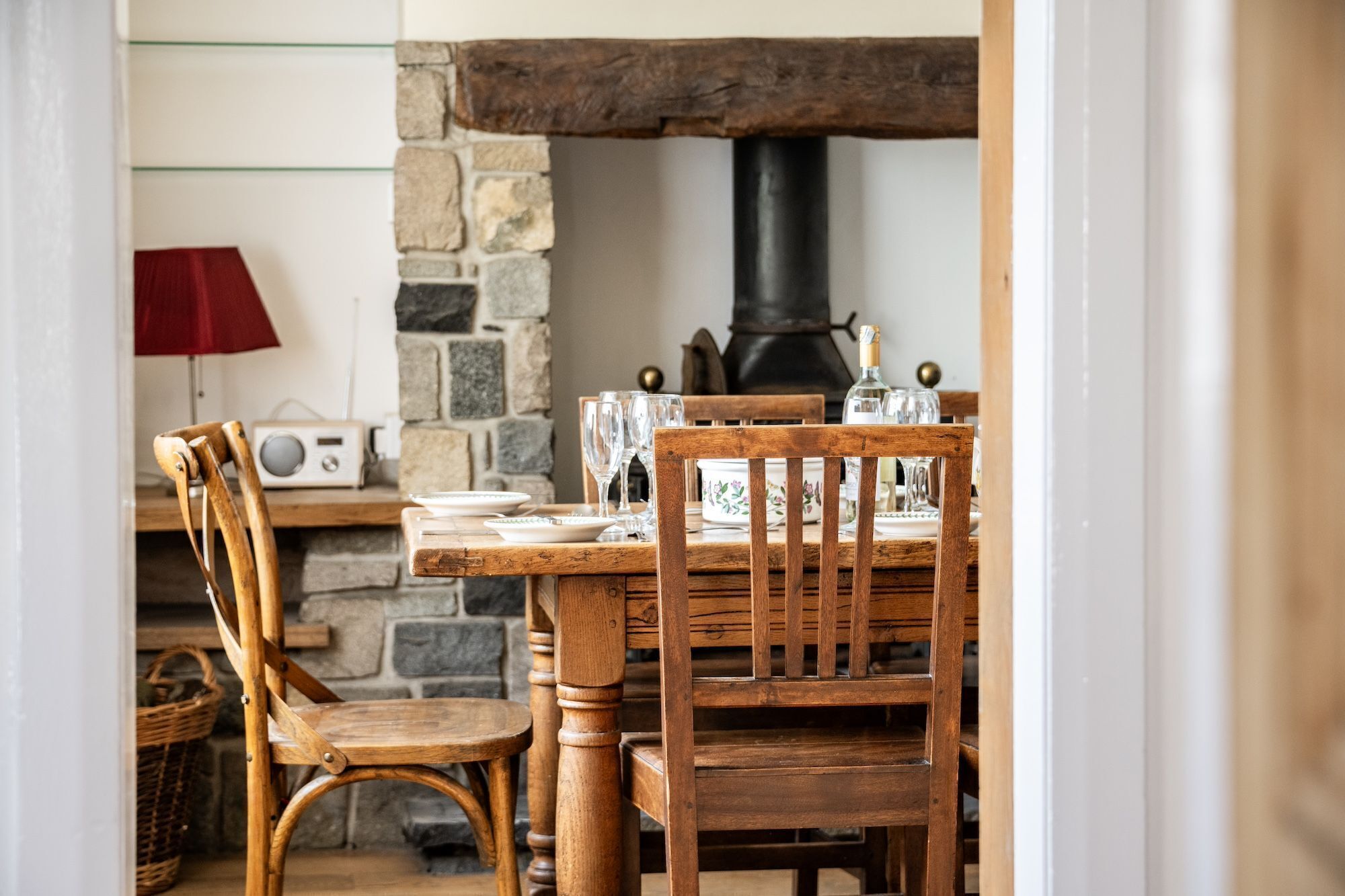 A rustic dining area with a stone fireplace, wooden chairs, and a table set for two.
