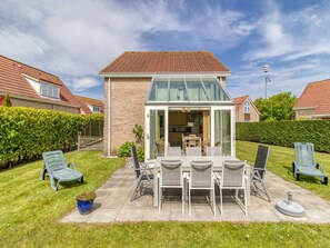 A house with a patio, a dining table with chairs, and a conservatory.