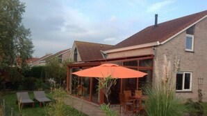 A house with a glass-enclosed patio, outdoor seating, and a lawn. - Scheldeveste 157 Breskens (Breskens)
