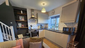 A modern kitchen with white cabinets, a stainless steel range hood, and a microwave. There's a wooden staircase leading to another level, and a small wooden rack near the sink. - Hidden Gem of Sheffield (Sheffield)