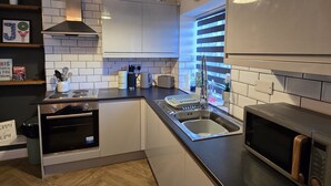 A modern kitchen with a wooden herringbone floor, stainless steel appliances, and a built-in oven. - Hidden Gem of Sheffield (Sheffield)