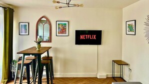 A modern living room with a wooden dining table, a TV mounted on the wall, and a unique ceiling light fixture. - Hidden Gem of Sheffield (Sheffield)