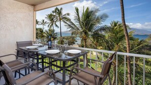 Un balcon avec une table dressée pour le dîner, donnant sur une plage bordée de palmiers et offrant une vue sur l’océan.