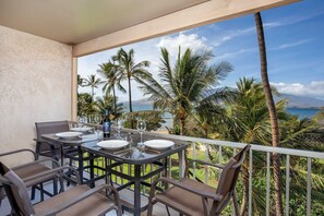 A balcony with a table set for dining, overlooking a beach with palm trees and a view of the ocean.