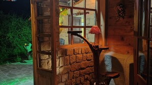 L’intérieur d’un chalet rustique en bois, avec un mur en pierre, une porte en bois, une fenêtre ornée d’une lampe rouge et un plafond en bois.