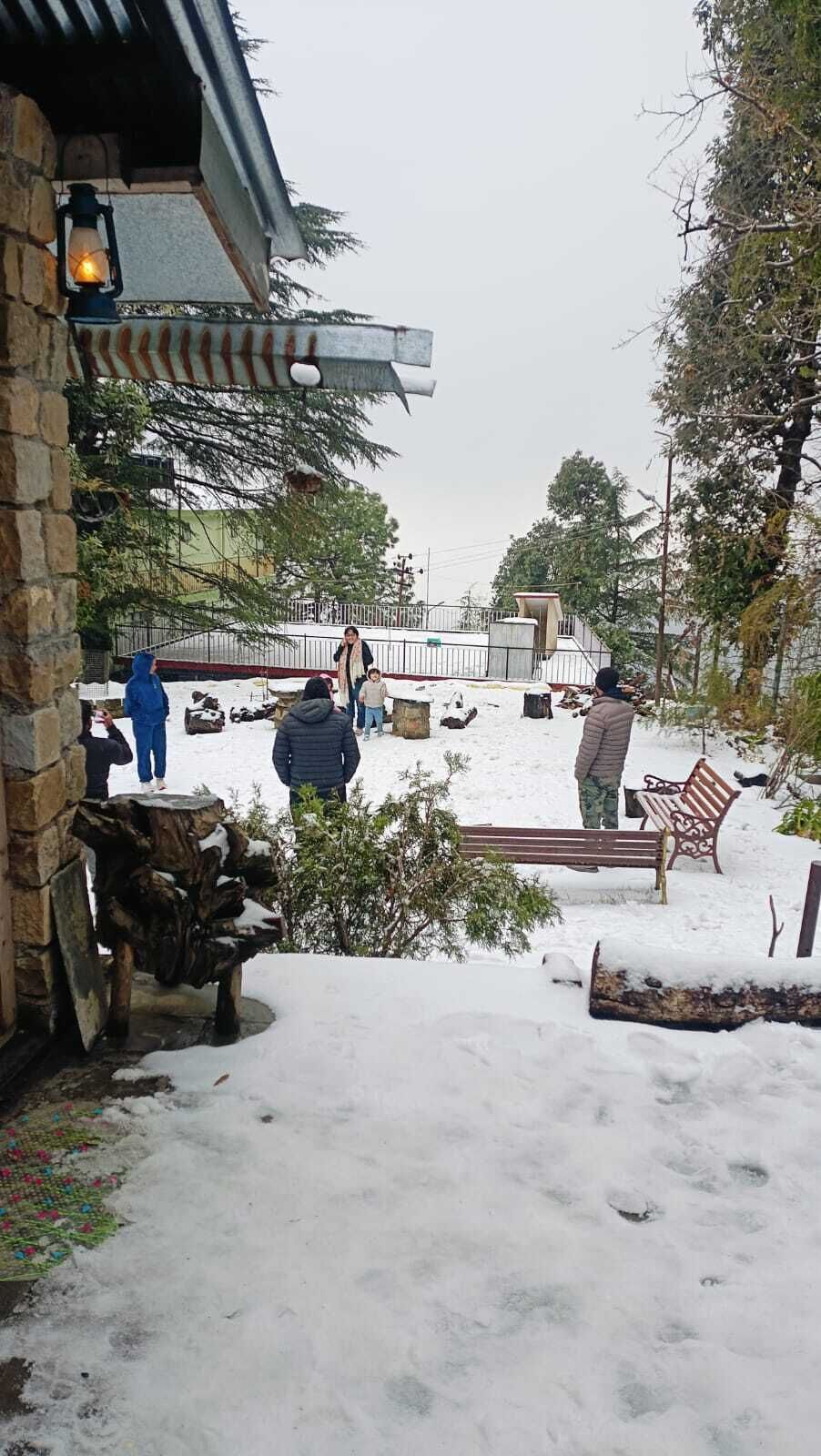 Un espacio exterior nevado con un muro de piedra, un banco y una valla metálica.