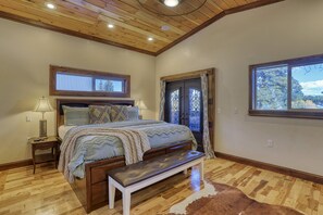 Un dormitorio con techo de madera, una cama grande con un banco, una ventana con cortinas y una puerta con herrajes decorativos.