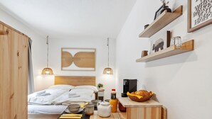 A compact, modern bedroom with a wooden bed, bedside table, and a small kitchenette area. - Promenade Apt 016 by Interhome (Arosa)