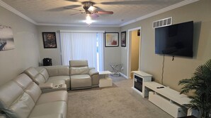 A living room with a sectional sofa, a ceiling fan, a flat-screen TV, and a potted plant.