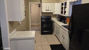 A compact kitchen with white cabinets, a black stove, and a refrigerator.