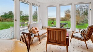 A sunlit room with large windows, a wooden deck, and outdoor furniture.