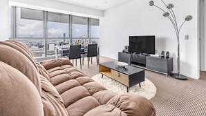 Een moderne woonkamer met een grote bank, een televisie en een eethoek met stoelen en een tafel.