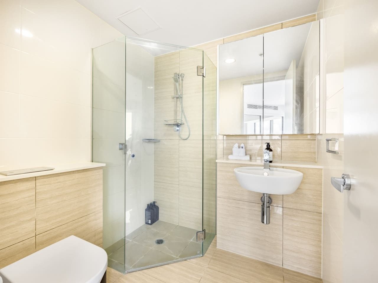 A modern bathroom with a glass-enclosed shower, a white sink, and wooden cabinetry.