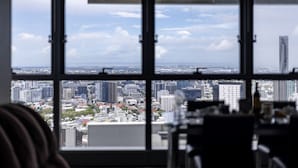 Uitzicht vanuit een hoog kantoorgebouw met grote ramen, waarop een stadsbeeld zichtbaar is met diverse gebouwen en een heldere lucht.